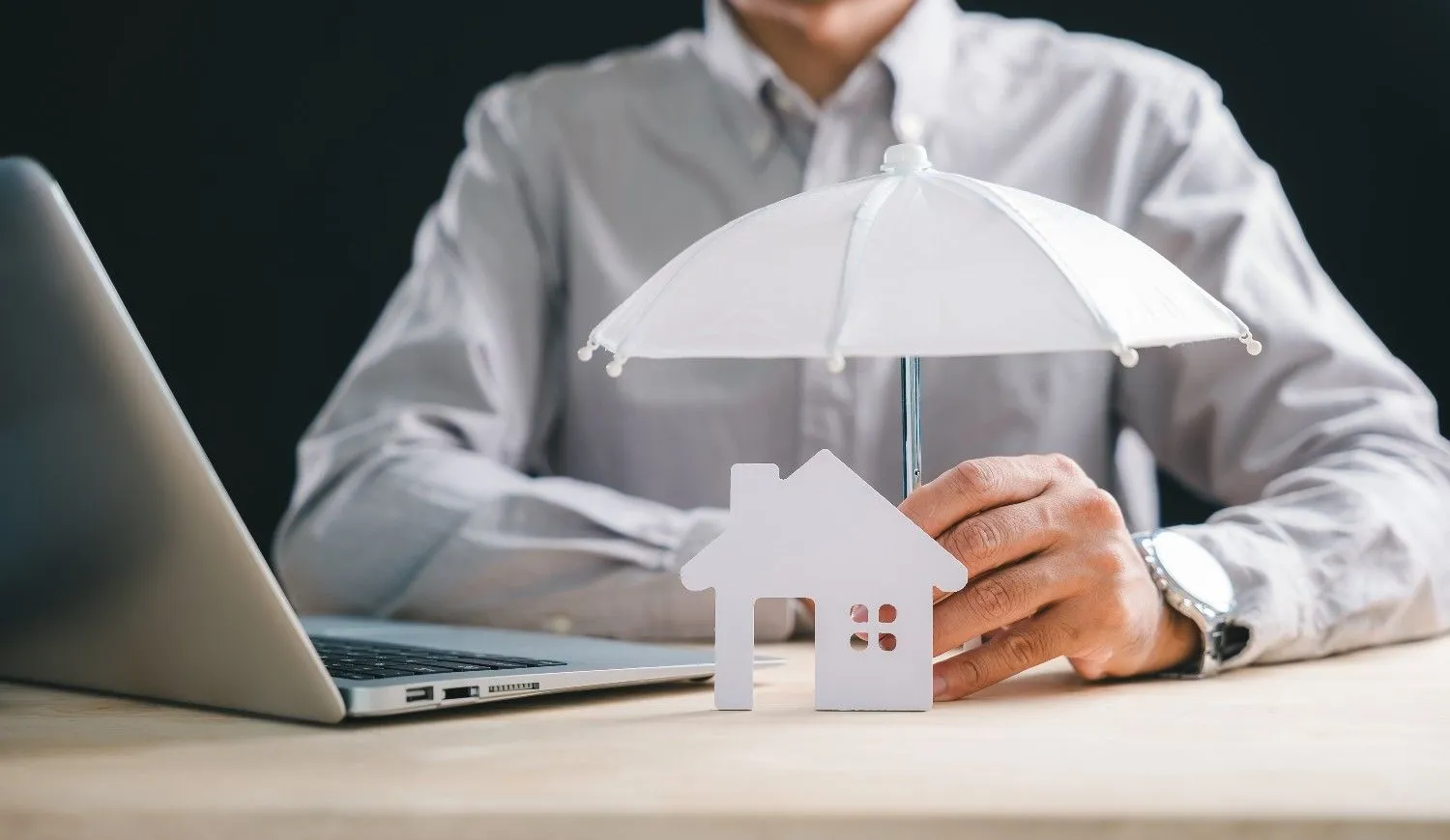 Small umbrella held over a white model house on a desk
